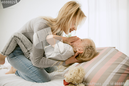 Image of Young mother and her little daughter hugging and kissing on bed