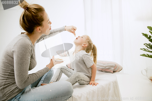 Image of Young mother and her little daughter hugging and kissing on bed