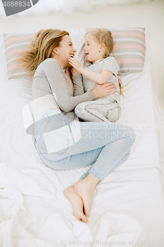 Image of Young mother and her little daughter hugging and kissing on bed