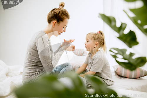 Image of Young mother and her little daughter hugging and kissing on bed