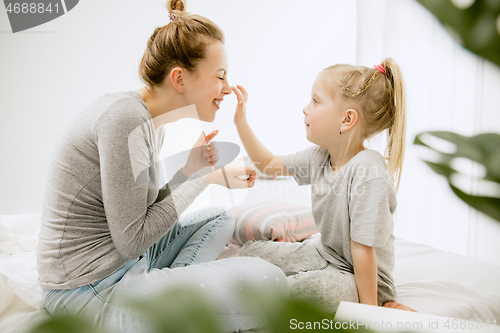 Image of Young mother and her little daughter hugging and kissing on bed