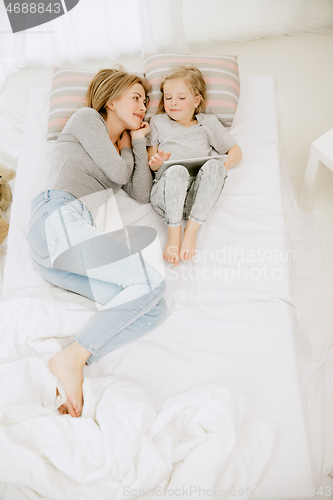 Image of Young mother and her little daughter hugging and kissing on bed