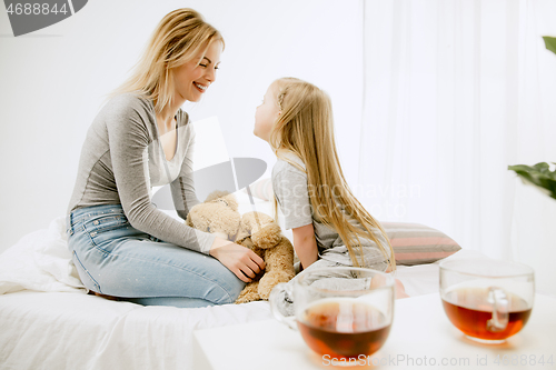 Image of Young mother and her little daughter hugging and kissing on bed