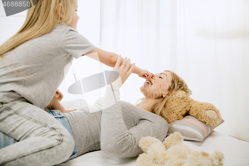 Image of Young mother and her little daughter hugging and kissing on bed