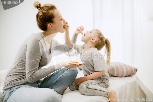 Image of Young mother and her little daughter hugging and kissing on bed