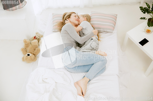 Image of Young mother and her little daughter hugging and kissing on bed