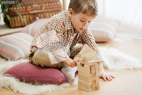 Image of Little child sitting on the floor. Pretty boy palying with wooden cubes at home