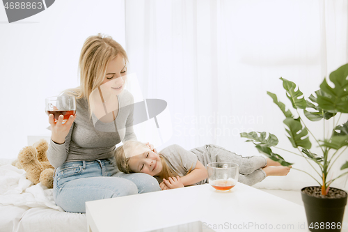 Image of Young mother and her little daughter hugging and kissing on bed