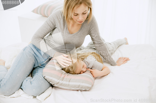 Image of Young mother and her little daughter hugging and kissing on bed