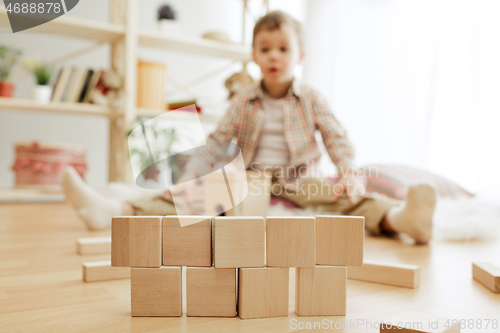 Image of Little child sitting on the floor. Pretty boy palying with wooden cubes at home