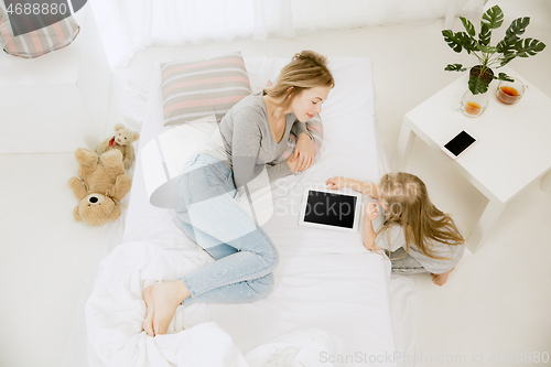 Image of Young mother and her little daughter hugging and kissing on bed