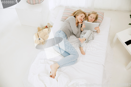 Image of Young mother and her little daughter hugging and kissing on bed