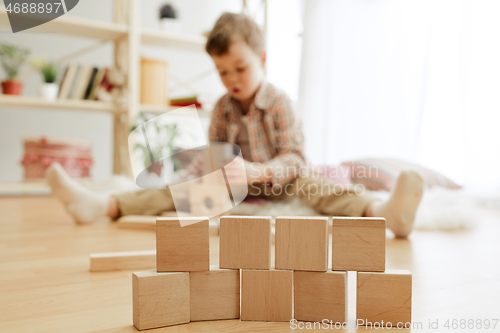 Image of Little child sitting on the floor. Pretty boy palying with wooden cubes at home