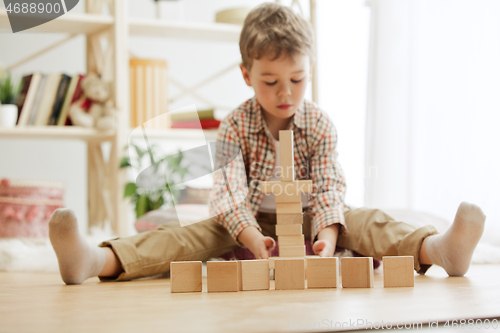 Image of Little child sitting on the floor. Pretty boy palying with wooden cubes at home