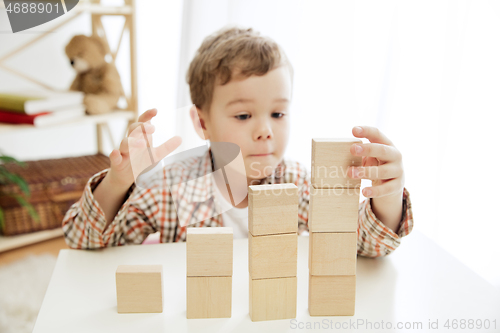 Image of Little child sitting on the floor. Pretty boy palying with wooden cubes at home