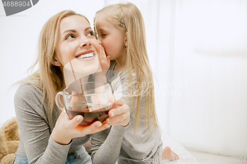 Image of Young mother and her little daughter hugging and kissing on bed