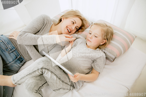 Image of Young mother and her little daughter hugging and kissing on bed