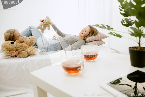 Image of Young mother and her little daughter hugging and kissing on bed