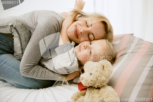 Image of Young mother and her little daughter hugging and kissing on bed