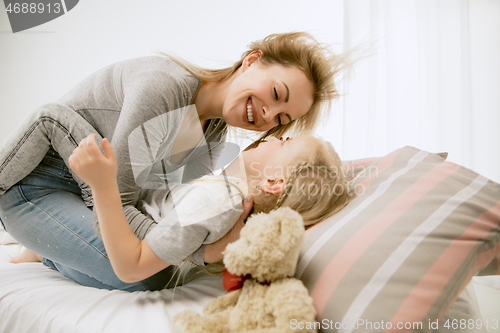 Image of Young mother and her little daughter hugging and kissing on bed