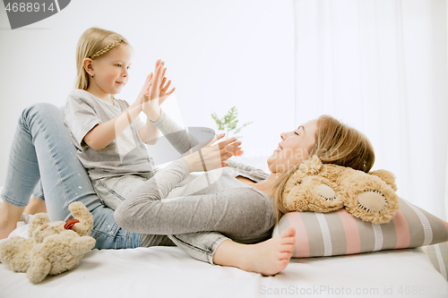 Image of Young mother and her little daughter hugging and kissing on bed