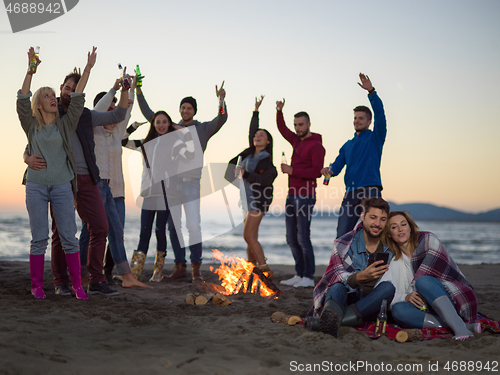 Image of Couple enjoying bonfire with friends on beach