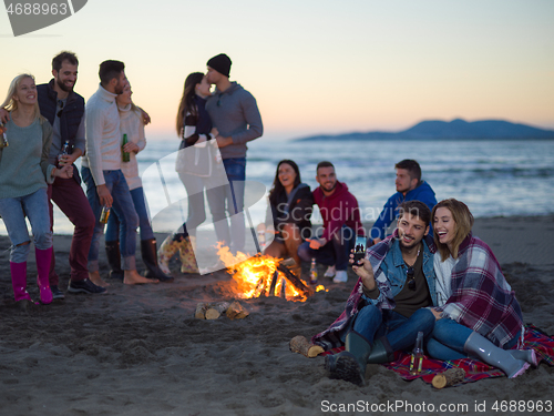Image of Couple enjoying bonfire with friends on beach
