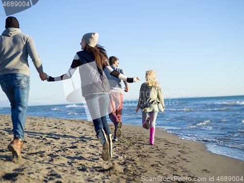 Image of Group of friends running on beach during autumn day