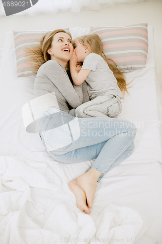 Image of Young mother and her little daughter hugging and kissing on bed