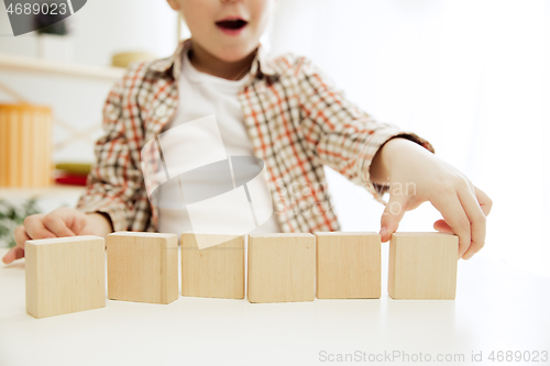 Image of Little child sitting on the floor. Pretty boy palying with wooden cubes at home