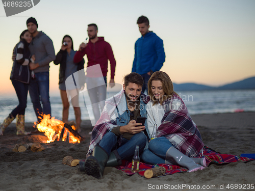 Image of Couple enjoying bonfire with friends on beach