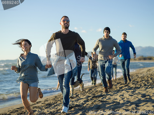 Image of Group of friends running on beach during autumn day