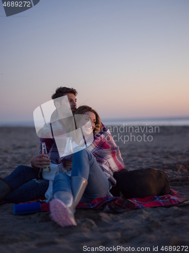 Image of Loving Young Couple Sitting On The Beach beside Campfire drinkin