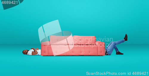 Image of Tall high man and long sofa isolated on blue studio background. Unusual delighted and long