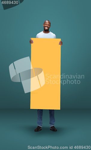 Image of Tall high man and long yellow banner isolated on blue studio background. Unusual delighted and long