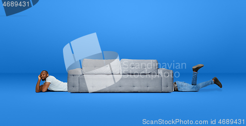 Image of Tall high man and long sofa isolated on blue studio background. Unusual delighted and long