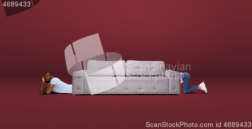 Image of Tall high man and long sofa isolated on red studio background. Unusual delighted and long