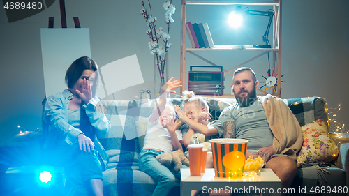 Image of Happy family watching projector, TV, movies with popcorn in the evening at home. Mother, father and kids spending time together.