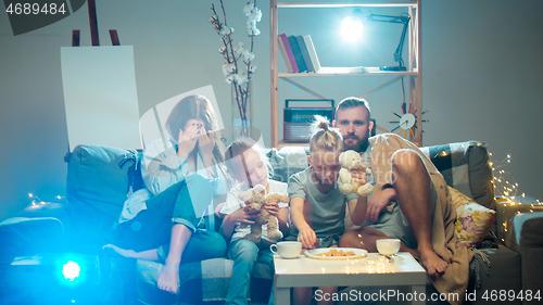 Image of Happy family watching projector, TV, movies with popcorn in the evening at home. Mother, father and kids spending time together.