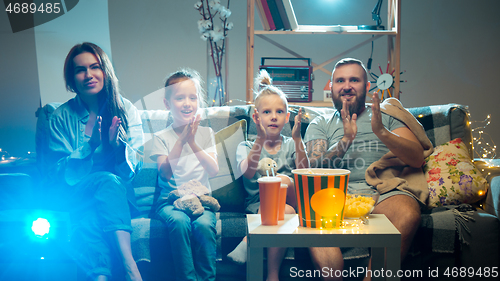 Image of Happy family watching projector, TV, movies with popcorn in the evening at home. Mother, father and kids spending time together.