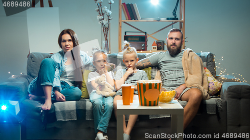 Image of Happy family watching projector, TV, movies with popcorn in the evening at home. Mother, father and kids spending time together.