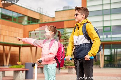 Image of happy school children with backpacks and scooters