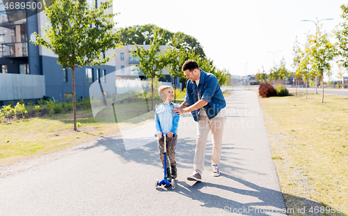 Image of happy father and little son riding scooter in city