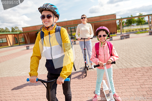 Image of happy school children with mother riding scooters