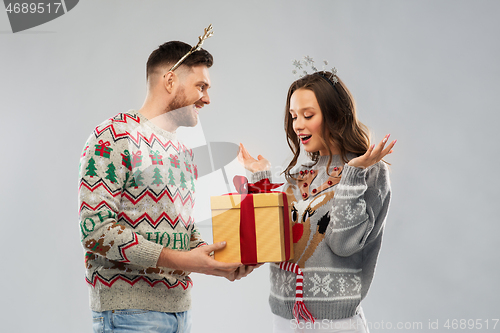 Image of happy couple in christmas sweaters with gift box