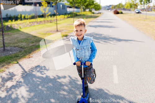 Image of happy little boy riding scooter in city