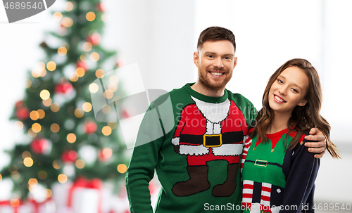 Image of happy couple in ugly sweaters over christmas tree