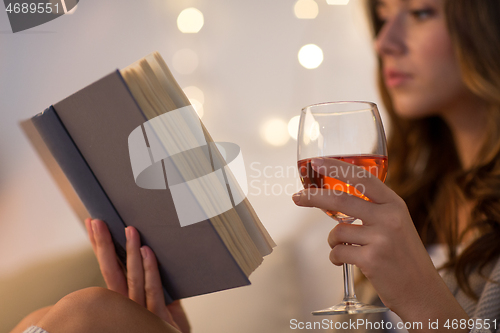 Image of close up of woman reading book and drinking wine