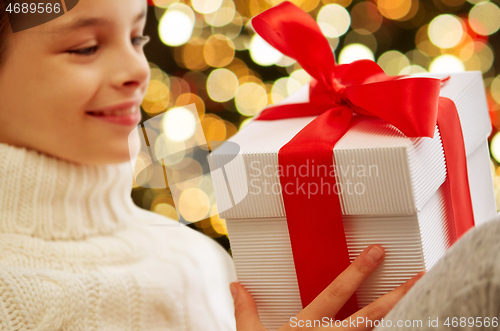Image of happy girl with christmas gift over festive lights