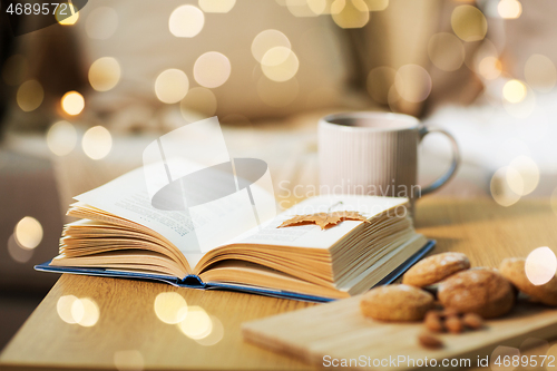 Image of book with autumn leaf, cookies and tea on table